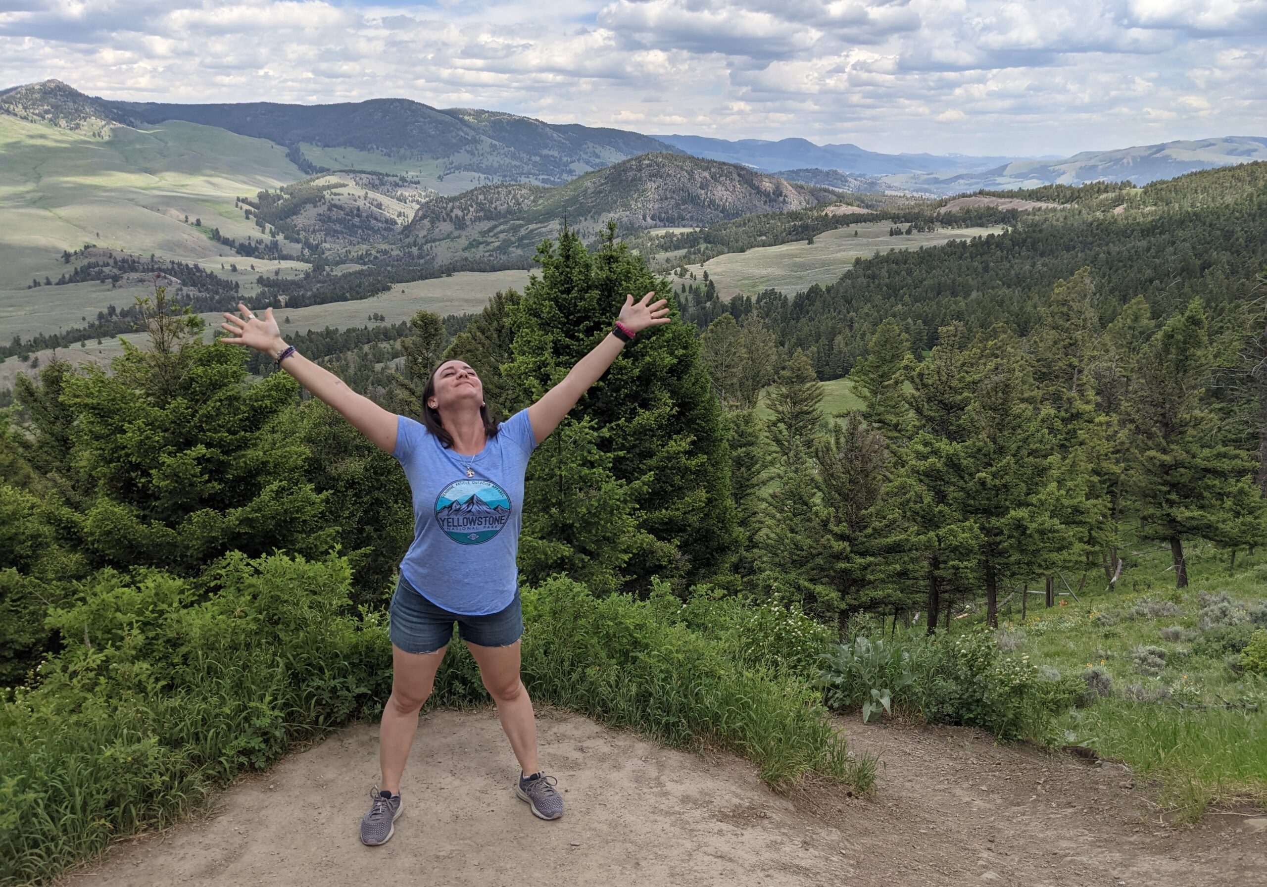 Social worker Lindsay Minarovic, LCSW-S stands on a mountainside smiling with her head back and her arms stretched up to the sky.