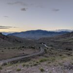 a road runs between hills against a blue mountain backdrop